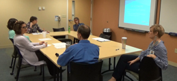 Image of people sitting around a square table talking